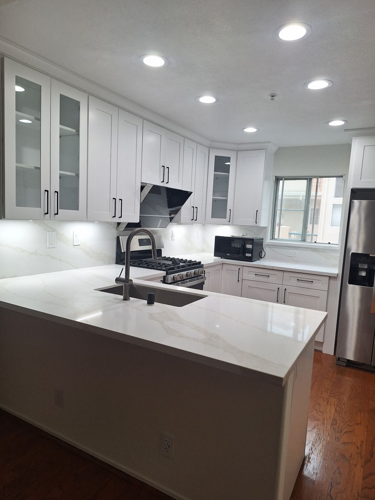 White shaker cabinets, quartz waterfall counter, full-height backsplash and recessed lights